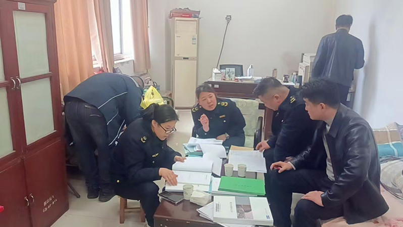 工作人员围坐桌前，对照文件资料进行业务交流与工作部署。