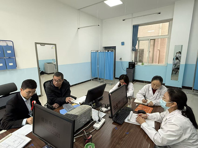 后勤安保处副处长康江龙（右）在卫生所工作会议现场，与参会人员交流健康学校建设及卫生所规范化管理相关工作内容。